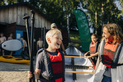 Happy boy with counselor wearing life jackets while going for kayaking at summer camp