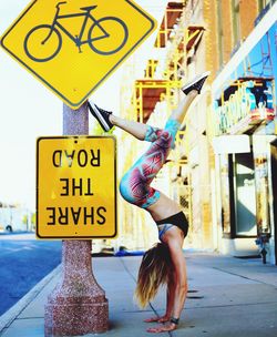 Full length of woman performing handstand on sidewalk in city