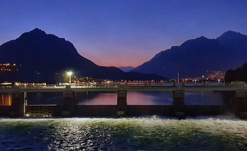 Illuminated city by river against clear sky at night