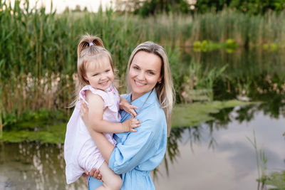 Portrait of young woman and toddler girl standing against lake