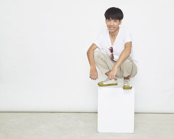 Portrait of a smiling young woman standing against white wall