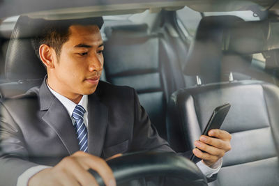 Businessman using phone seen through windshield while driving car