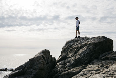 Man standing on rock by sea against sky