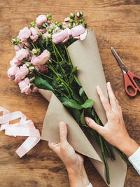 Top view on wooden table with roses, scissors, craft paper and pink ribbon. florist work place.