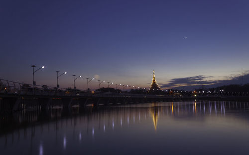 Illuminated buildings by river against sky at night