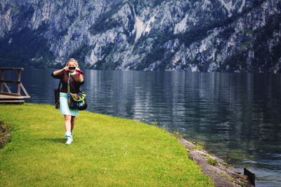 Young woman photographing at lakeshore by mountain