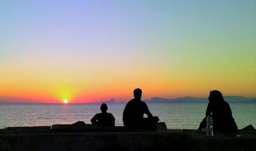 Silhouette people looking at sea against sky during sunset