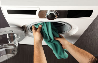 Cropped hands of man putting clothes in washing machine at home