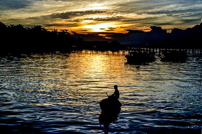 Silhouette man on lake against sky during sunset
