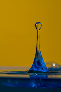 Close-up of water drop on glass against yellow background