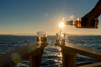 Close-up of hand pouring drink against sea