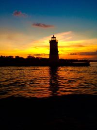 Silhouette lighthouse by sea against sky during sunset