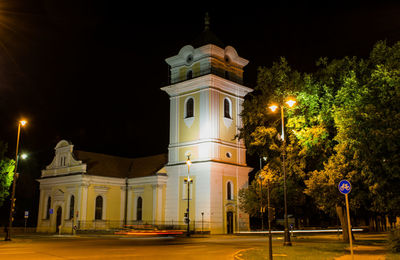 Illuminated street by building against sky at night