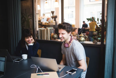 Smiling female and male creative professionals discussing over laptop at desk in office