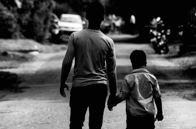 Rear view of father and son holding hands while walking on road
