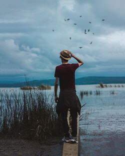 Rear view of man standing at beach against sky