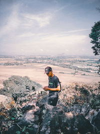 Side view of young man on rock against sky