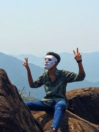 Full length of young woman sitting on mountain against sky