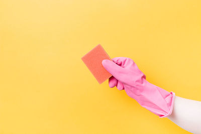 Hand in pink rubber glove holds orange sponge for washing dishes and cleaning, cleaning concept