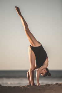 Full length of woman exercising at beach against sky