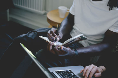 Midsection of businessman writing in diary while colleague using laptop in creative office