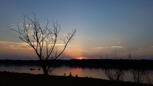 Silhouette bare tree by lake against sky during sunset