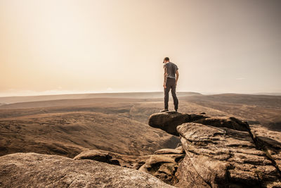 Man standing on rock looking at camera against sky