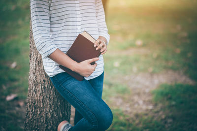 Midsection of woman holding tree trunk in park