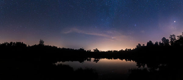 Silhouette trees by lake against sky at night