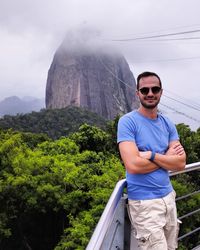 Portrait of handsome young man standing at observation point against mountain