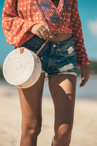 Girl walks along the beach with a rattan bag on her shoulder