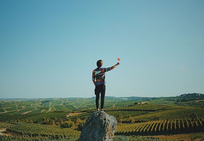 Young man with arms raised standing against clear sky