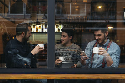 Colleagues talking while sitting in cafe seen through window