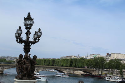 Statue by river in city against sky