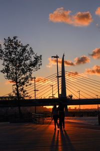 Silhouette people walking on footpath against sky during sunset