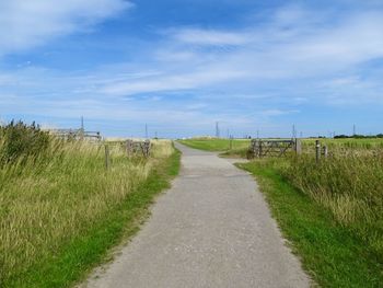 Empty road amidst field against sky