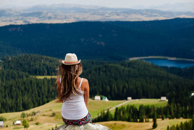 Rear view of woman sitting on rock against mountains