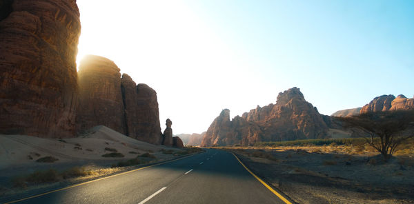 Road leading towards mountains against clear sky