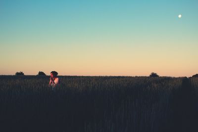 Woman standing at farm against clear blue sky during sunset