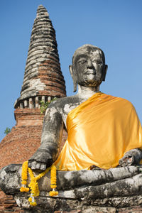 Low angle view of buddha statue and stupa against clear blue sky