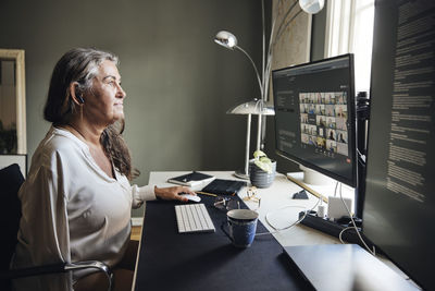 Businesswoman doing video conference through computer while sitting at desk in home office