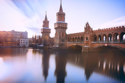 Reflection of oberbaumbruecke in river against sky on sunny day