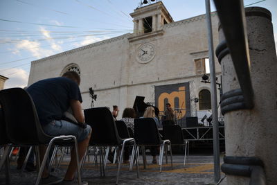 Rear view of people sitting on chair outside building