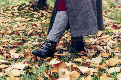 Low section of woman standing on dry leaves during autumn