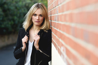 Portrait of young woman standing by brick wall