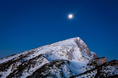 Low angle view of snowcapped mountain against blue sky