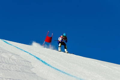 Low angle view of people skiing on snowcapped mountain against clear blue sky