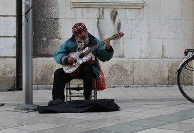 Street musician playing guitar while sitting outdoors