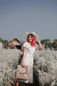 Young woman standing amidst flowers against clear sky