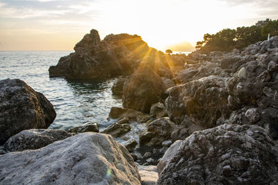 Rocks on beach against sky during sunset